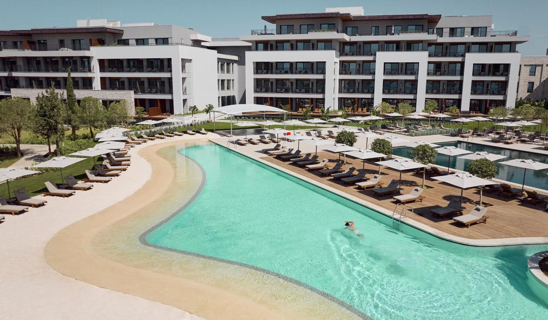 Anda Barut Collection viesnīcas galvenā ēka un lielais āra baseins ar sauļošanās krēsliem, saulessargiem un koka terasēm