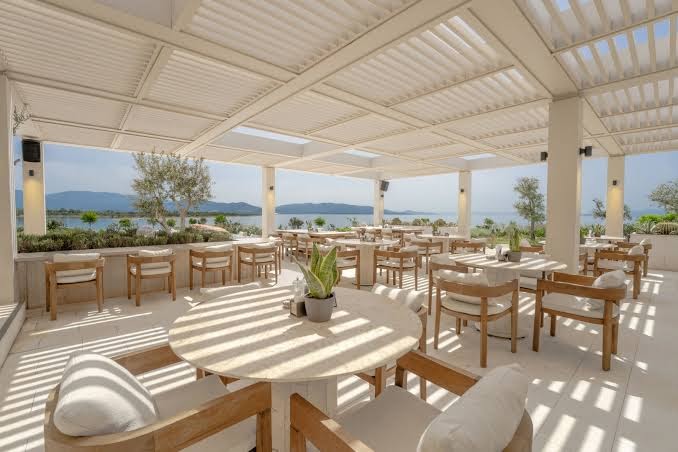 Anda Barut Collection modernā restorāna terase ar skatu uz jūru — gaišs interjers, koka mēbeles un eleganta nojume
