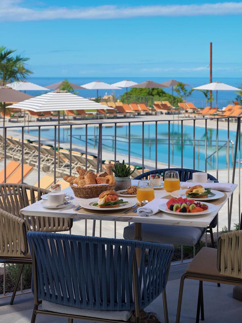 Gran Hotel Taoro brokastu galds uz terases ar skatu uz baseinu un zilo okeānu, servētas olas, augļi un maize.