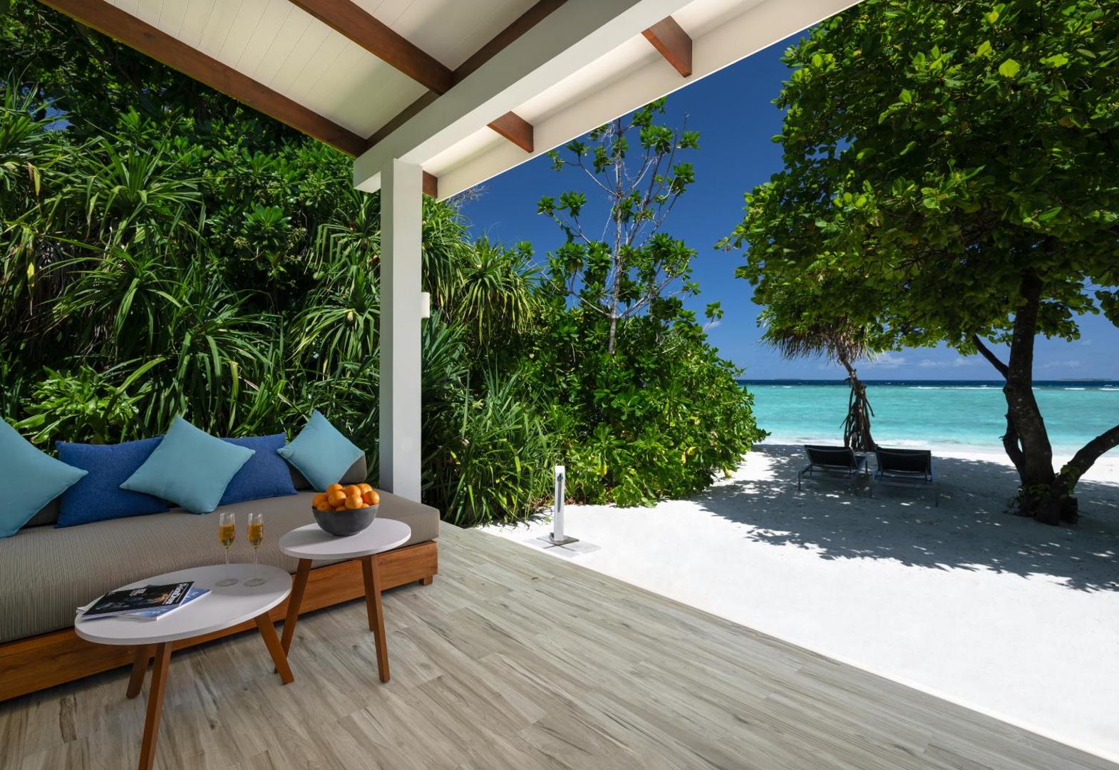 Ifuru Island Maldives privātā terase ar atpūtas dīvānu un skatu uz Indijas okeānu — tirkīza ūdens un tropu koki