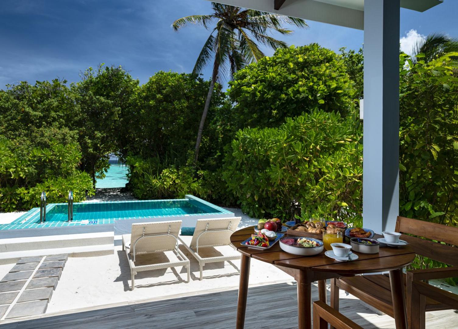 Brokastis uz Ifuru Island Maldives villas terases — galds ar augļiem un kafiju pie privātā baseina un okeāna krasta