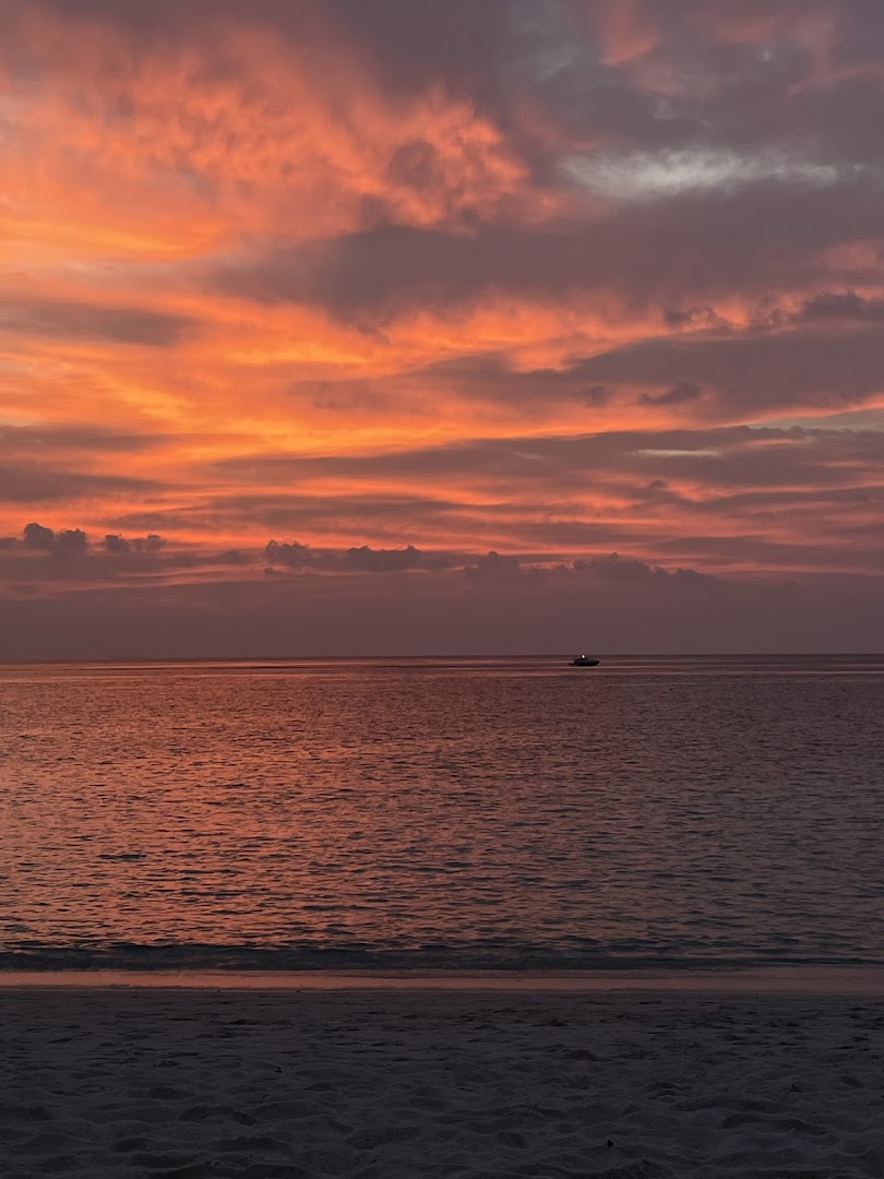 Dramatiskas oranžas un sārtas debesis saulrietā virs okeāna Ifuru Island Maldives kūrortā ar tālumā redzamu laivu