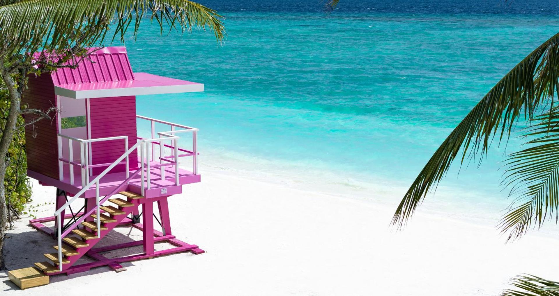 Ifuru Island Maldives koši rozā glābēju tornis baltu smilšu pludmalē pie tirkīzzila okeāna — tropu ainava ar palmām