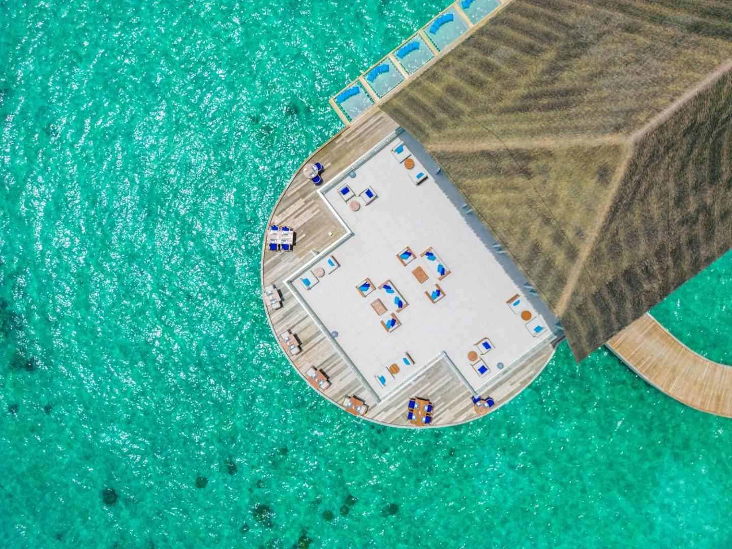 Ifuru Island Maldives restorāna terases skats no augšas, koka klājs ar galdiņiem virs dzidra, gaiši zila okeāna ūdens