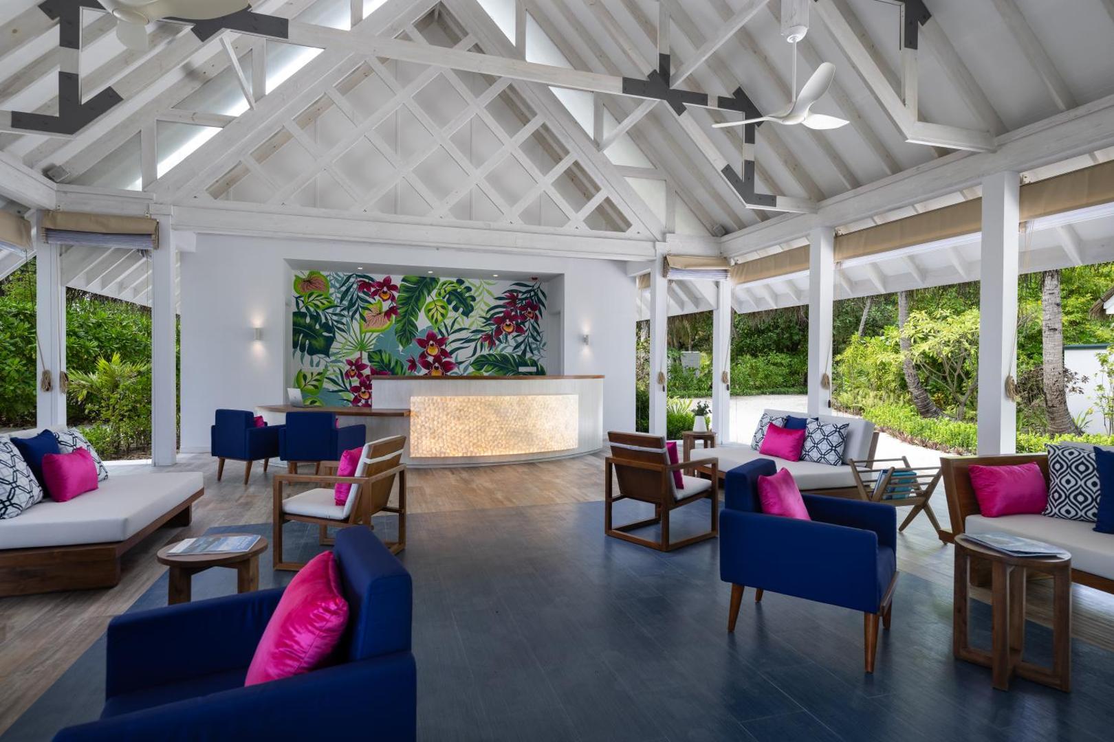 Ifuru Island Maldives viesnīcas lobby zona ar modernām mēbelēm, augstiem griestiem un koši ziliem un rozā akcentiem