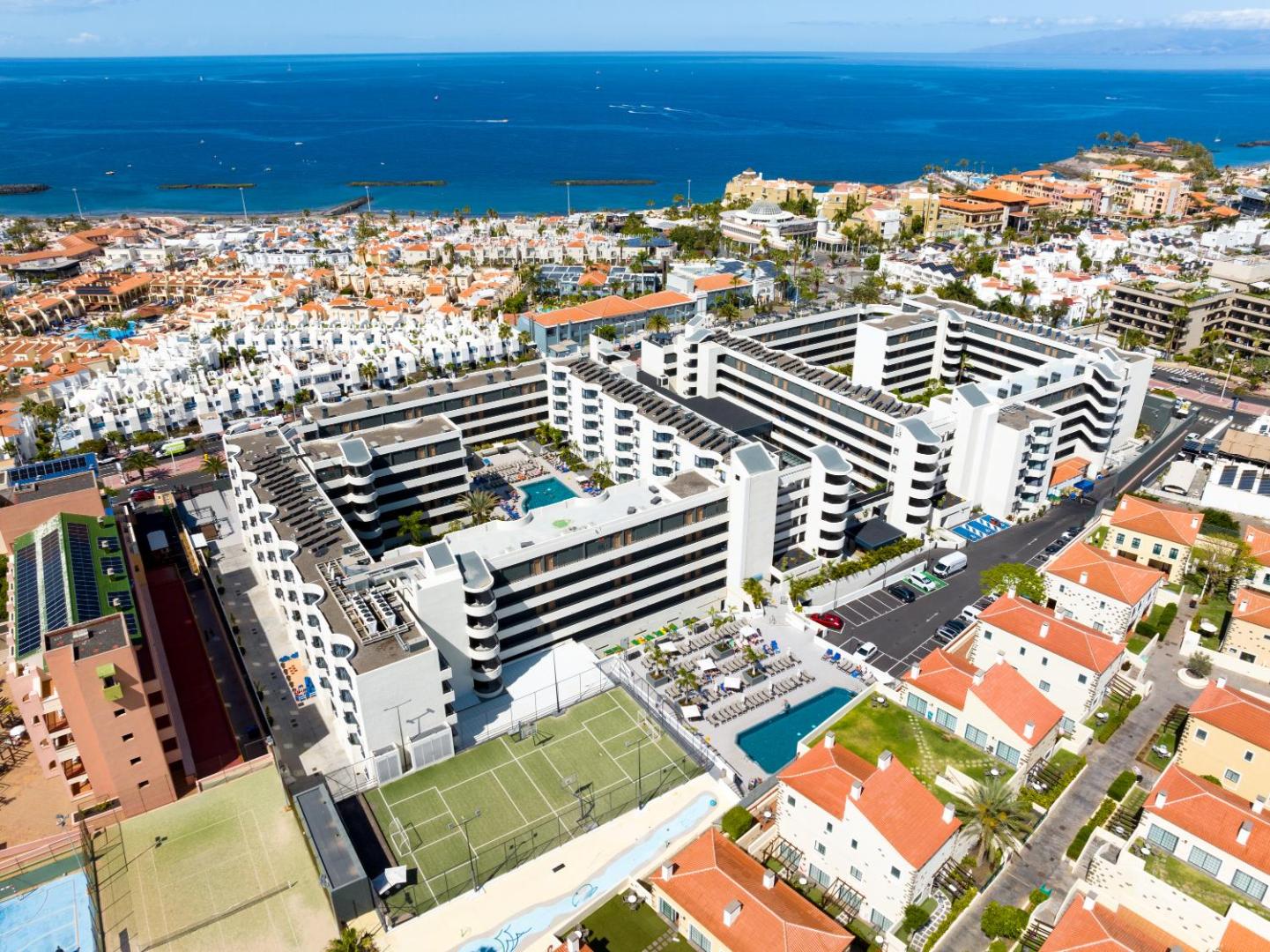 Hovima Suites Costa Adeje viesnīcas panorāmas skats no putna lidojuma Tenerifē — redzami baseini, tenisa korti un tuvums okeāna piekrastei