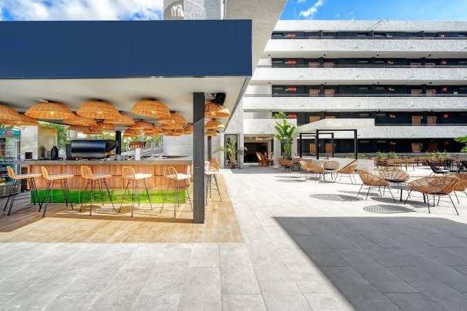 Hovima Suite Costa Adeje āra bārs ar stilīgiem pītiem gaismekļiem un koka krēsliem pie letes saulainā terasē Tenerifē