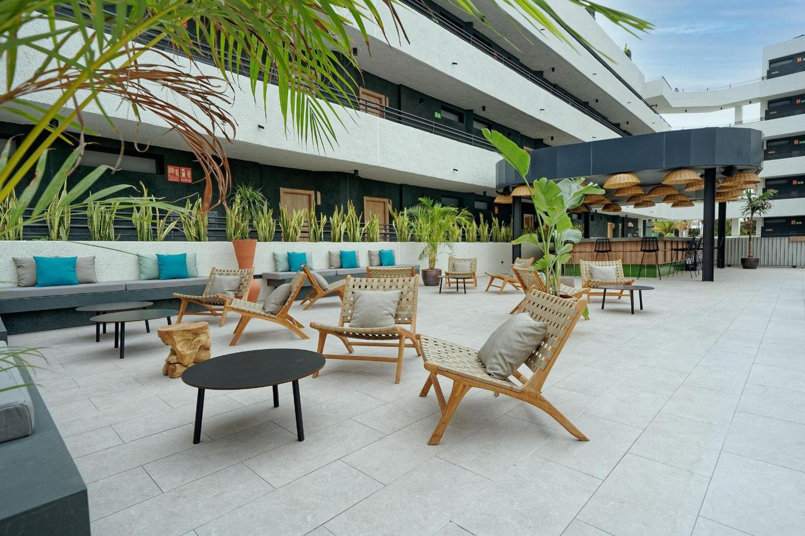 Hovima Suite Costa Adeje atpūtas zona ar koka krēsliem, mīkstiem spilveniem un palmām uz plašas viesnīcas terases
