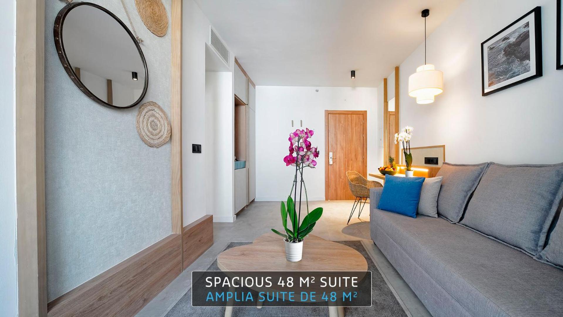 Hovima Suite Costa Adeje suite numura dzīvojamā zona ar pelēku dīvānu, koka galdiņu un orhideju podiņā
