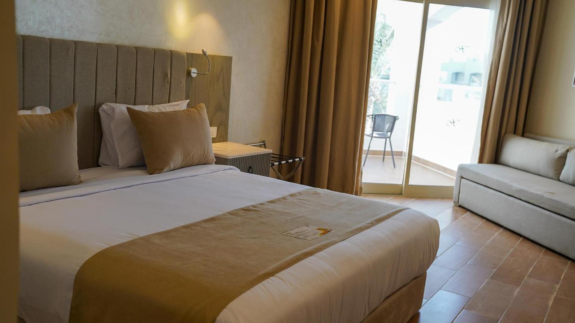 Xanadu Club Makadi Bay numurs ar plašu gultu, dīvānu un izeju uz balkonu, no kura paveras skats uz teritoriju.