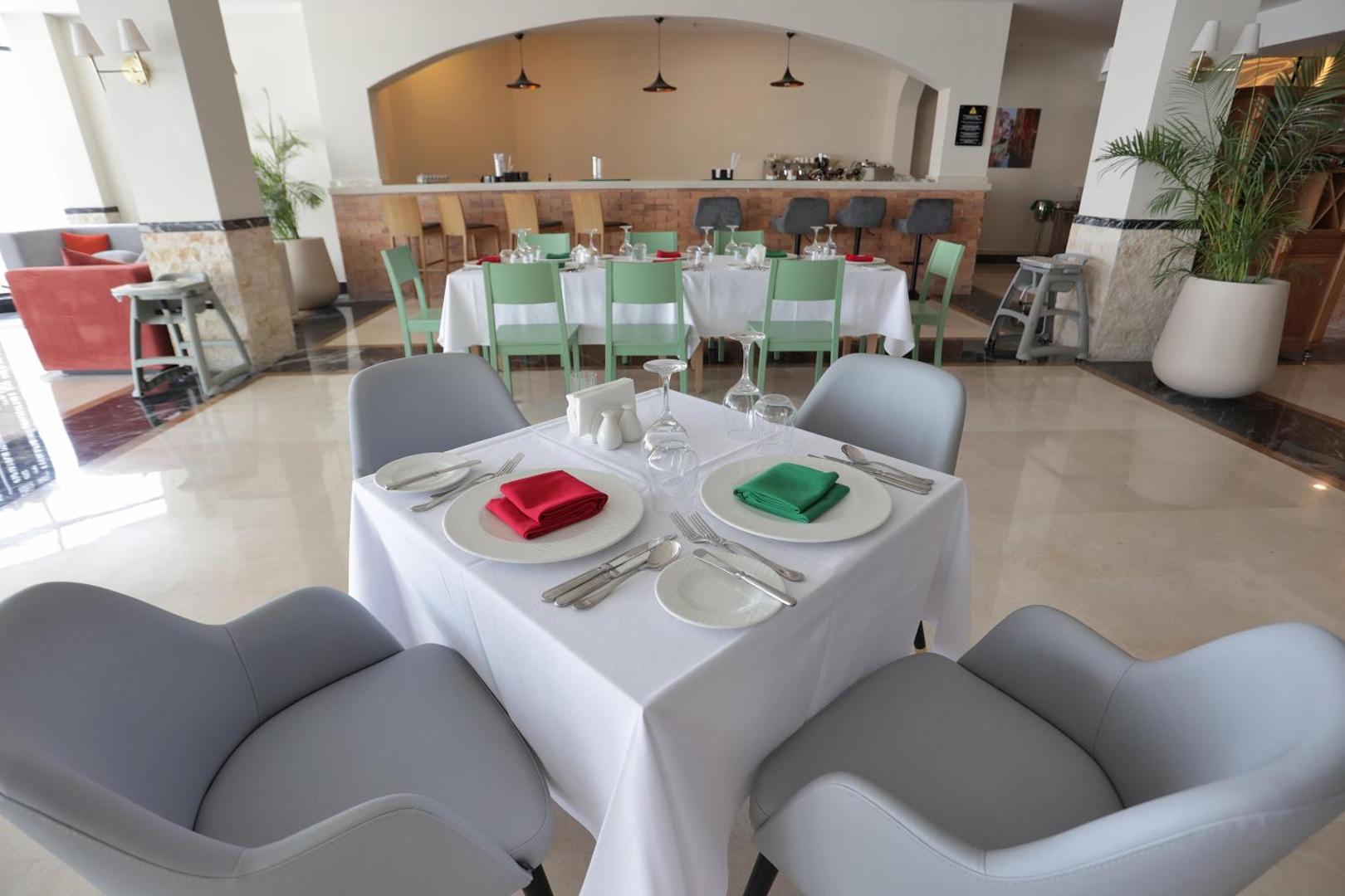 Xanadu Club Makadi Bay moderns restorāns ar gaišām mēbelēm un bāra zonu fonā — klāti galdi ar krāsainām salvetēm
