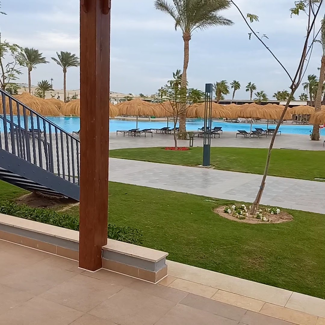 Skats no terases uz Xanadu Club Makadi Bay dārzu un baseina zonu ar salmu saulessargiem un palmām