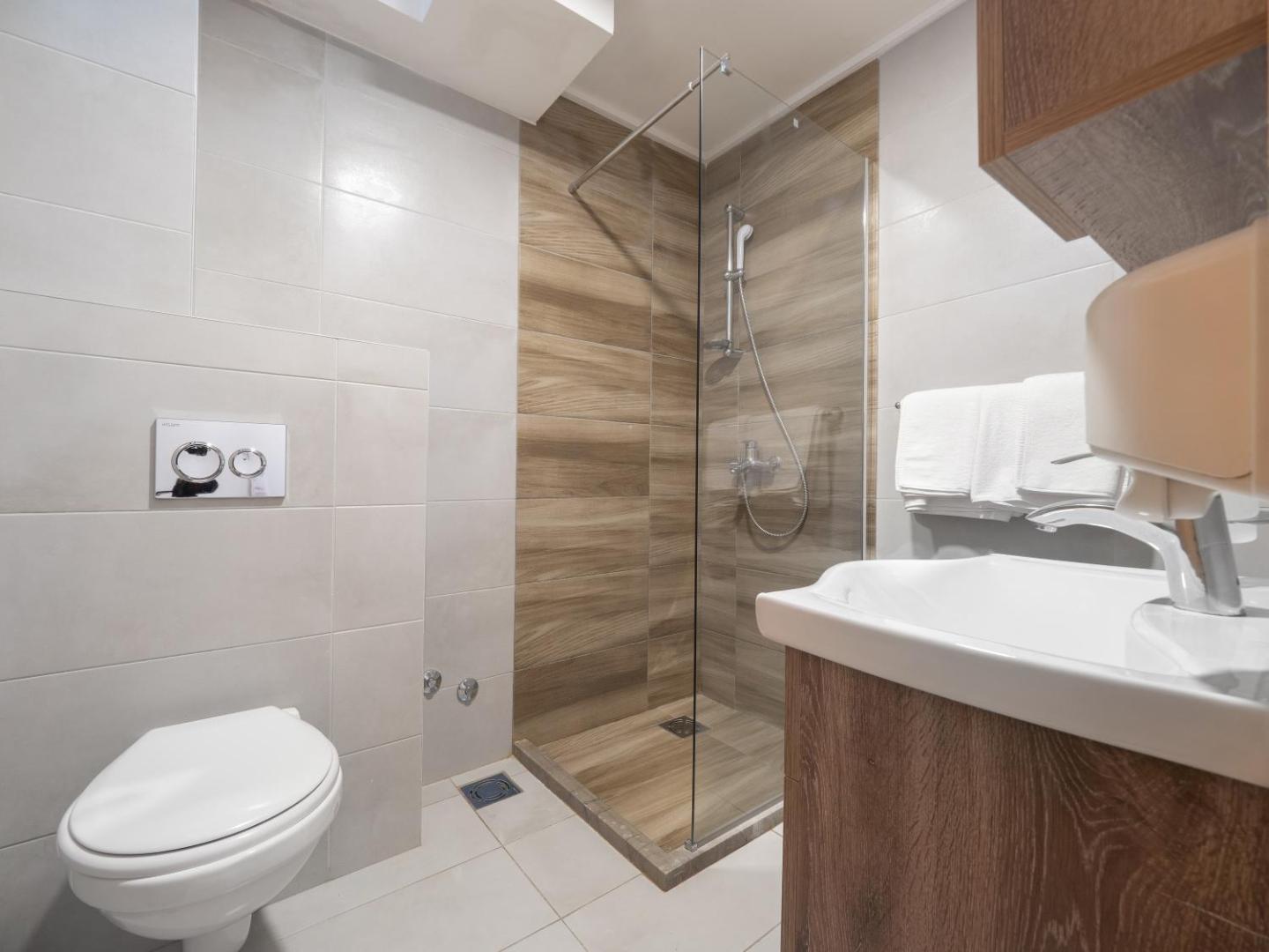 Gaišs un funkcionāls Hotel Tara numura vannas istabas interjers ar dušas kabīni un koka tekstūras elementiem