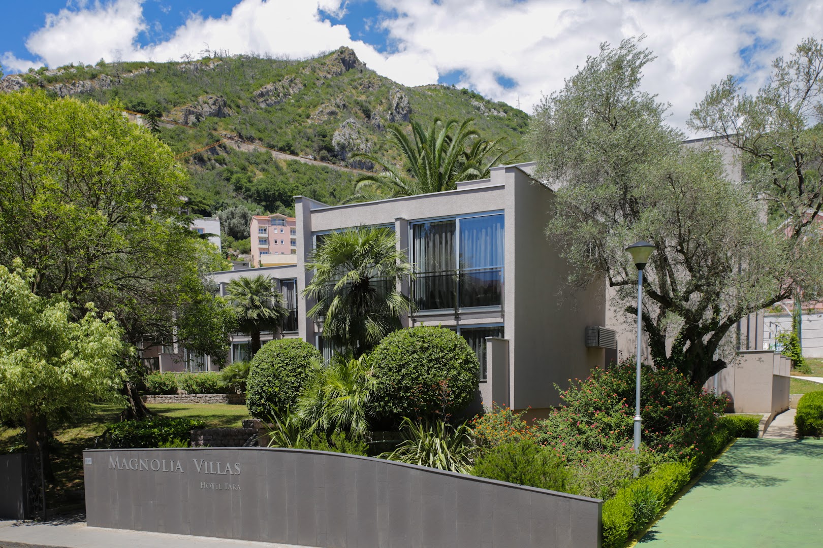 Hotel Tara Magnolia Villas komplekss Melnkalnē — modernas divstāvu villas ar palmām un kalnu fonu dārzā