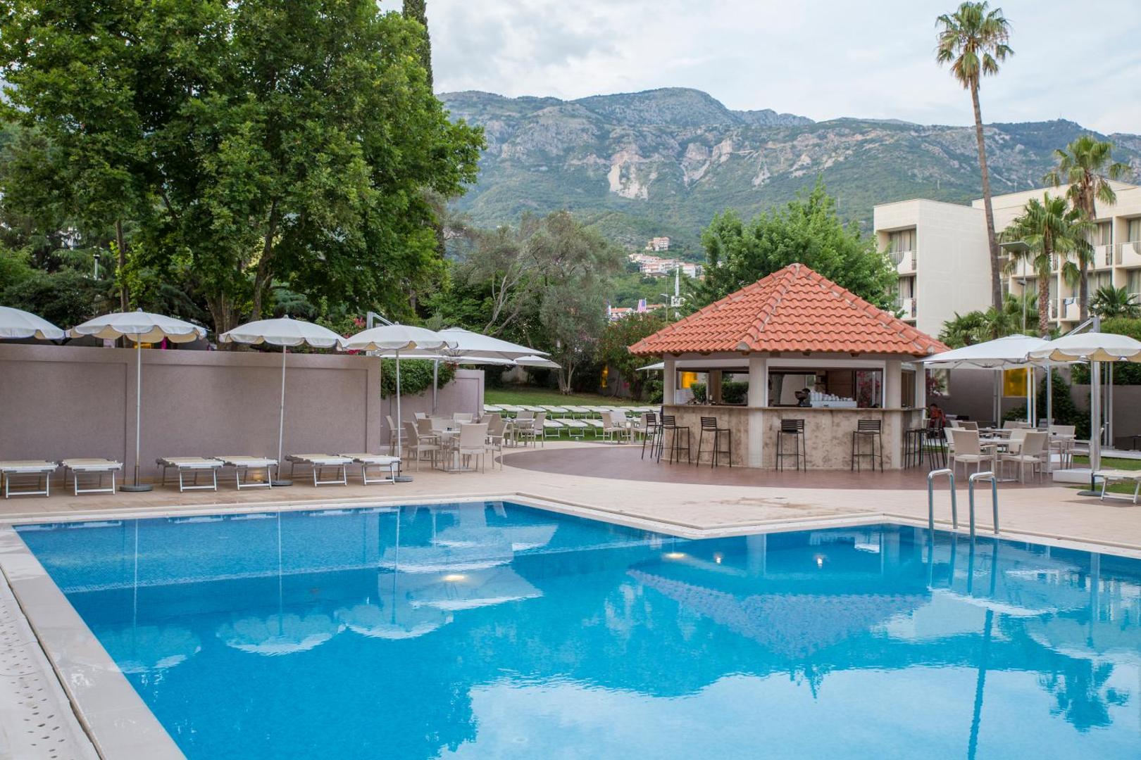 Hotel Tara āra baseins ar bāru un kalnu skatu Bečiči kūrortā — atpūtas zona ar saulessargiem un zaļojošu dārzu fonā