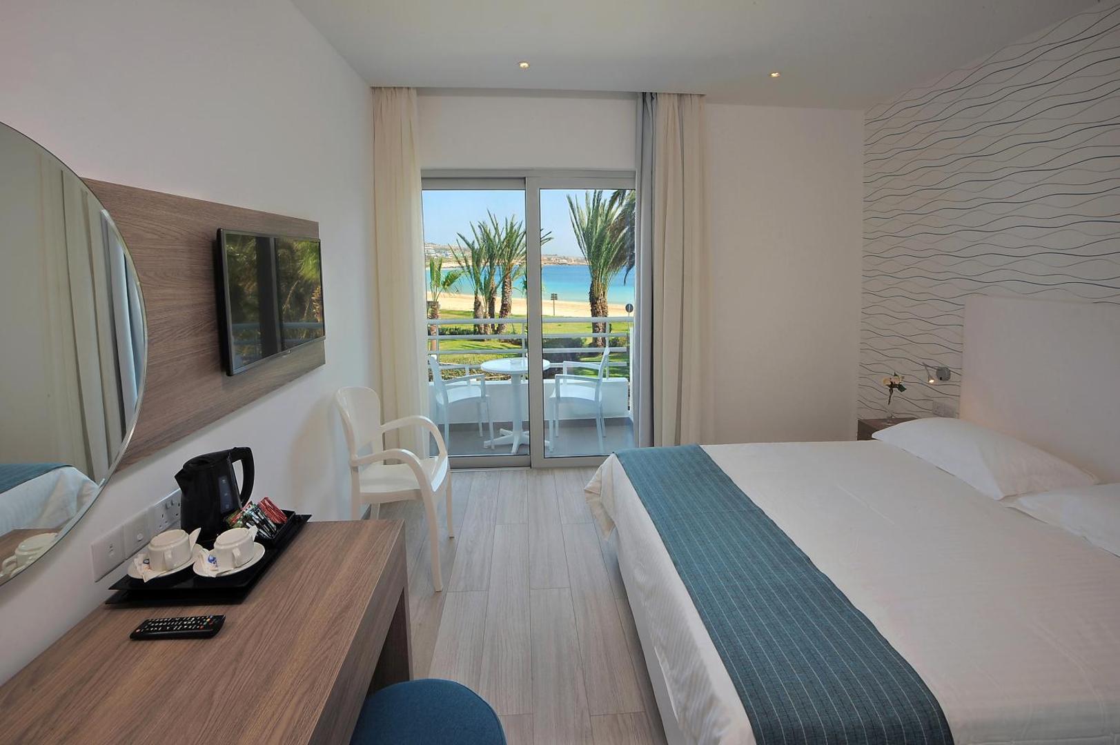Okeanos Beach Boutique gaišs numurs ar balkonu, no kura paveras skats uz palmām un pludmali Ajanapas piekrastē