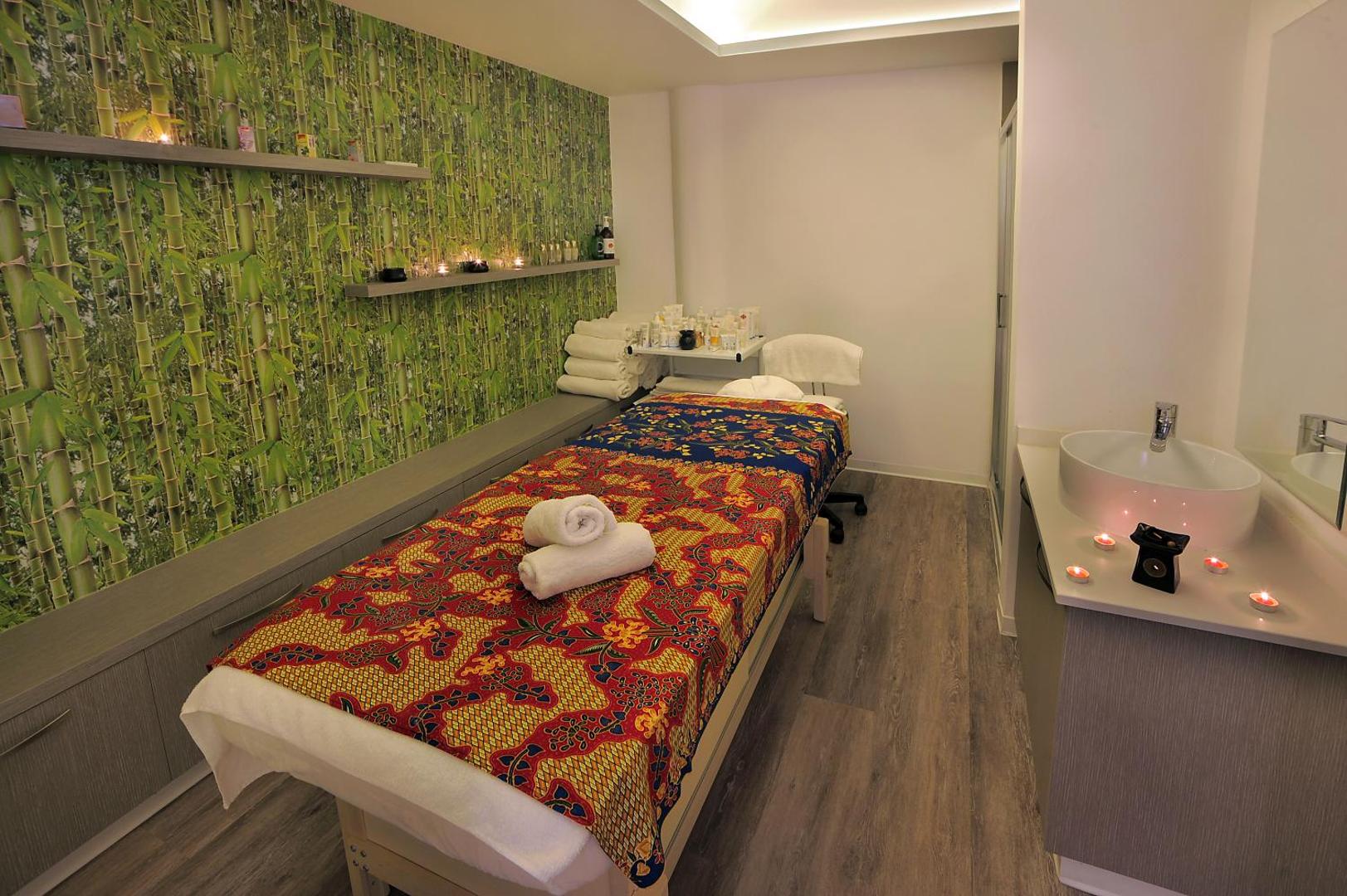 Okeanos Beach Boutique spa centra masāžas telpa ar bambusa raksta sienu, svecēm un profesionālu procedūru galdu Kiprā