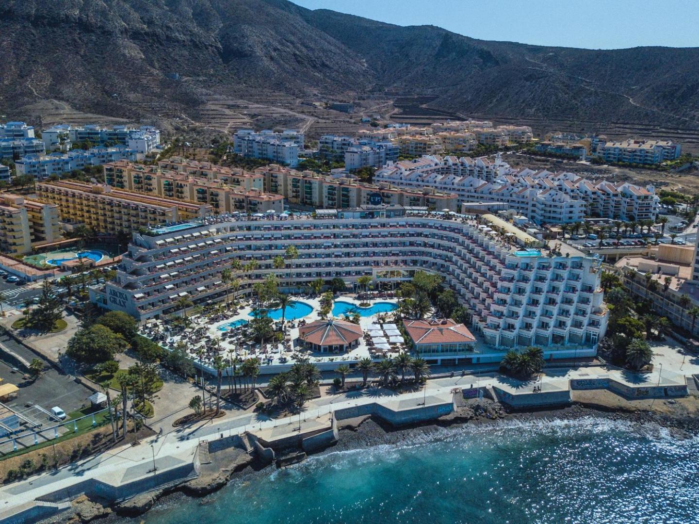 Arona Gran Hotel & Spa panorāmas skats no okeāna puses uz viesnīcas ēku, baseiniem un apkārtējo pilsētas ainavu Tenerifē