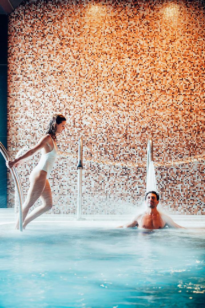 Arona Gran Hotel & Spa iekštelpu baseins ar hidromasāžas kaskādēm — viesi bauda ūdens procedūras pie mozaīkas flīžu sienas