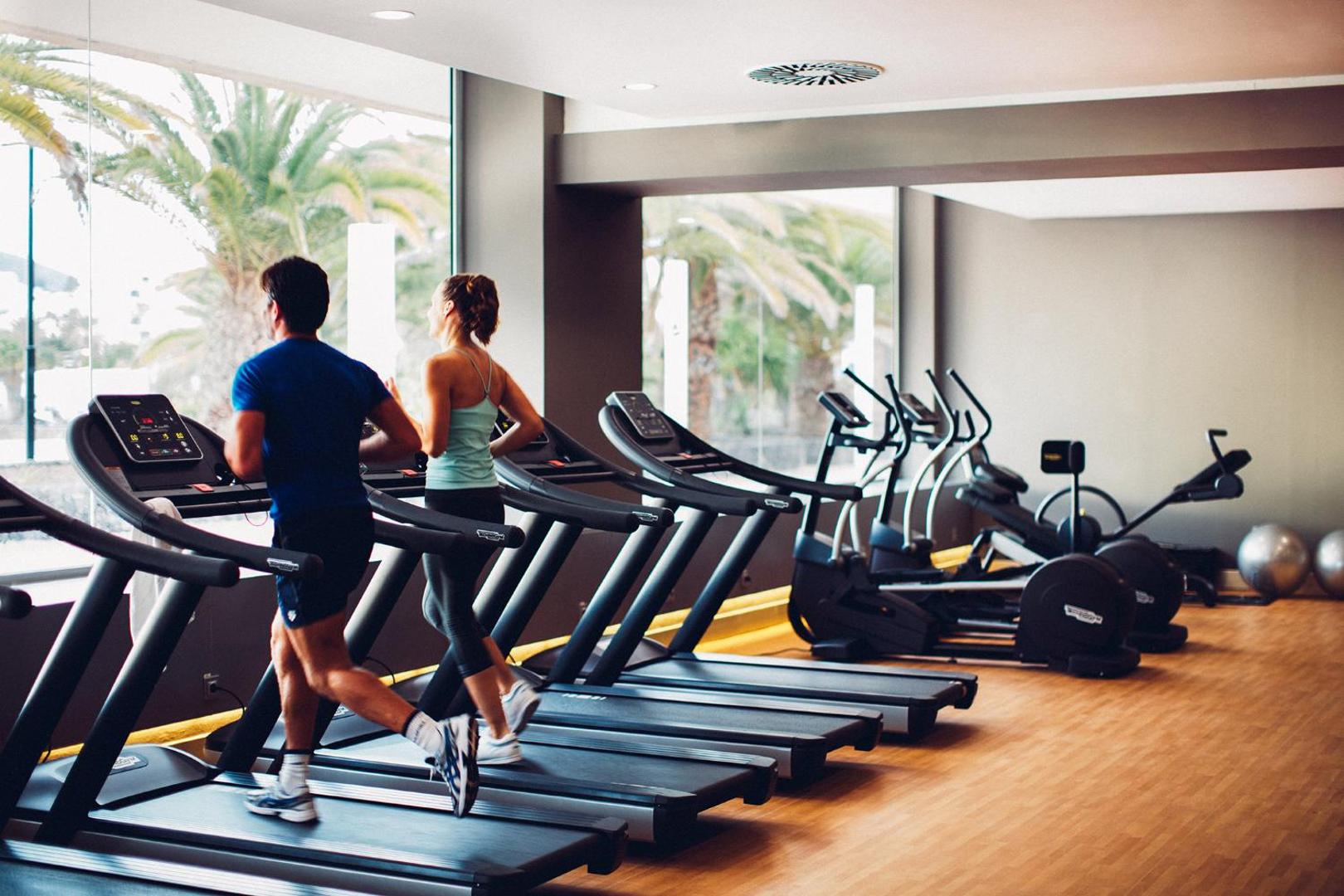 Arona Gran Hotel & Spa moderns fitness centrs ar skatu uz palmām — vairāki skrejceliņi un trenažieri aktīvai atpūtai Tenerifē