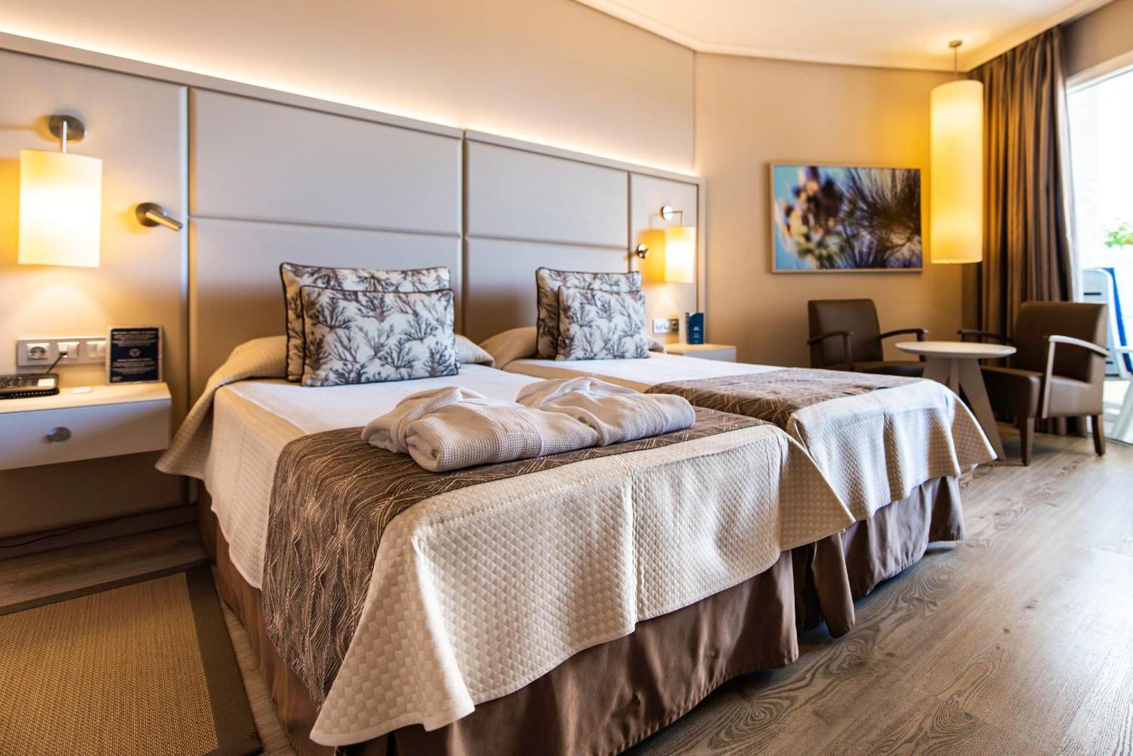 Arona Gran Hotel & Spa gaišs divvietīgs numurs ar modernu interjeru, koka grīdu un atpūtas zonu pie loga