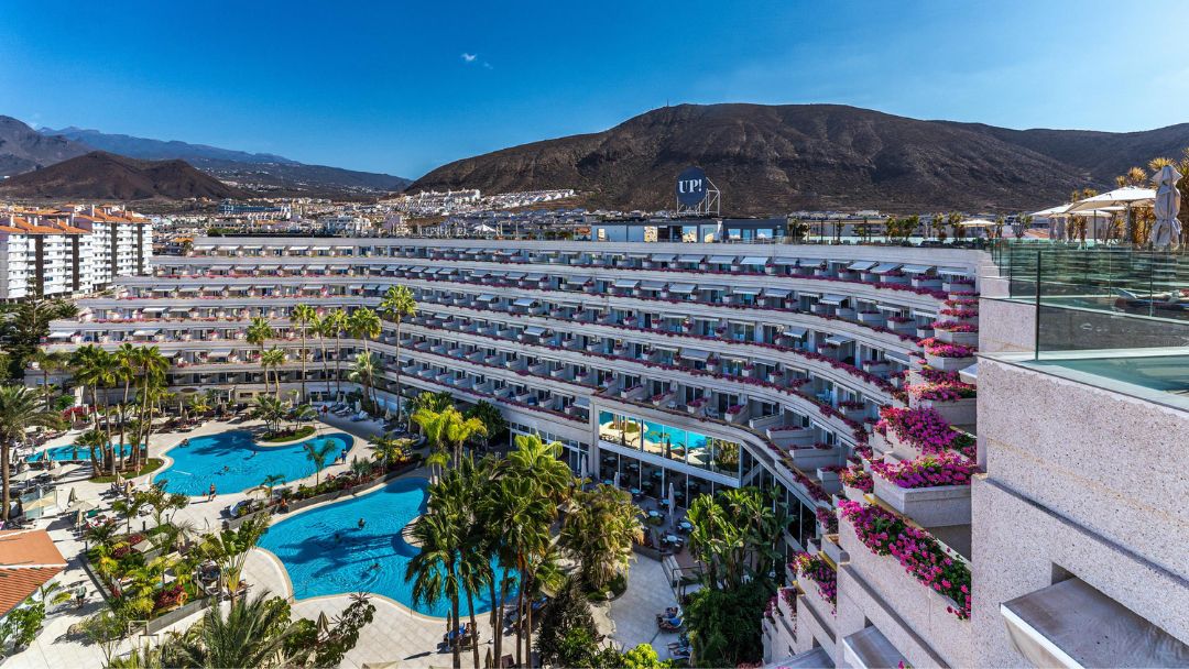 Arona Gran Hotel & Spa fasāde ar balkoniem un ziedošiem augiem, skats uz baseinu un kalniem fonā Los Kristianosā