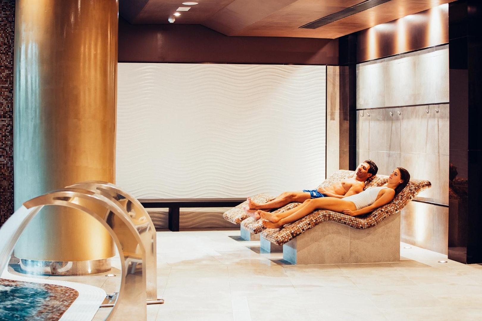 Arona Gran Hotel & Spa relaksācijas zona ar apsildāmiem mozaīkas zviļņiem — pāris atpūšas modernā spa centrā Tenerifē