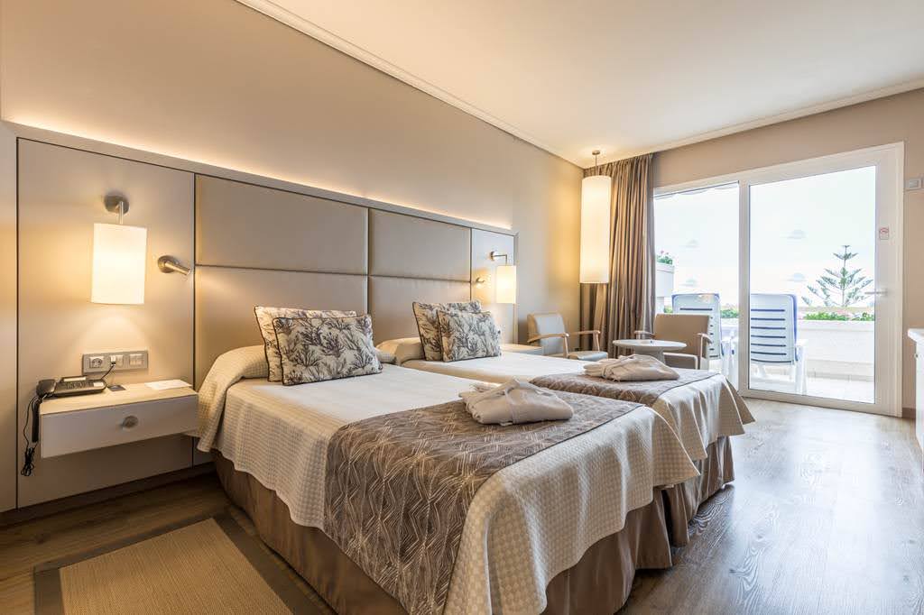 Arona Gran Hotel & Spa numurs ar divām gultām, halātiem un izeju uz terasi, kur redzami sauļošanās krēsli