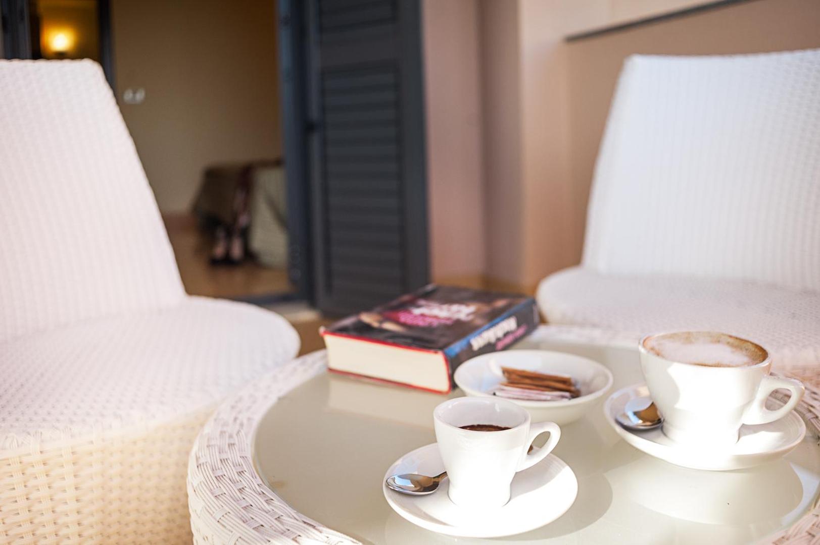 Kafijas tases un grāmata uz Rada Siri Hotel numura terases galdiņa ar pītiem krēsliem fonā