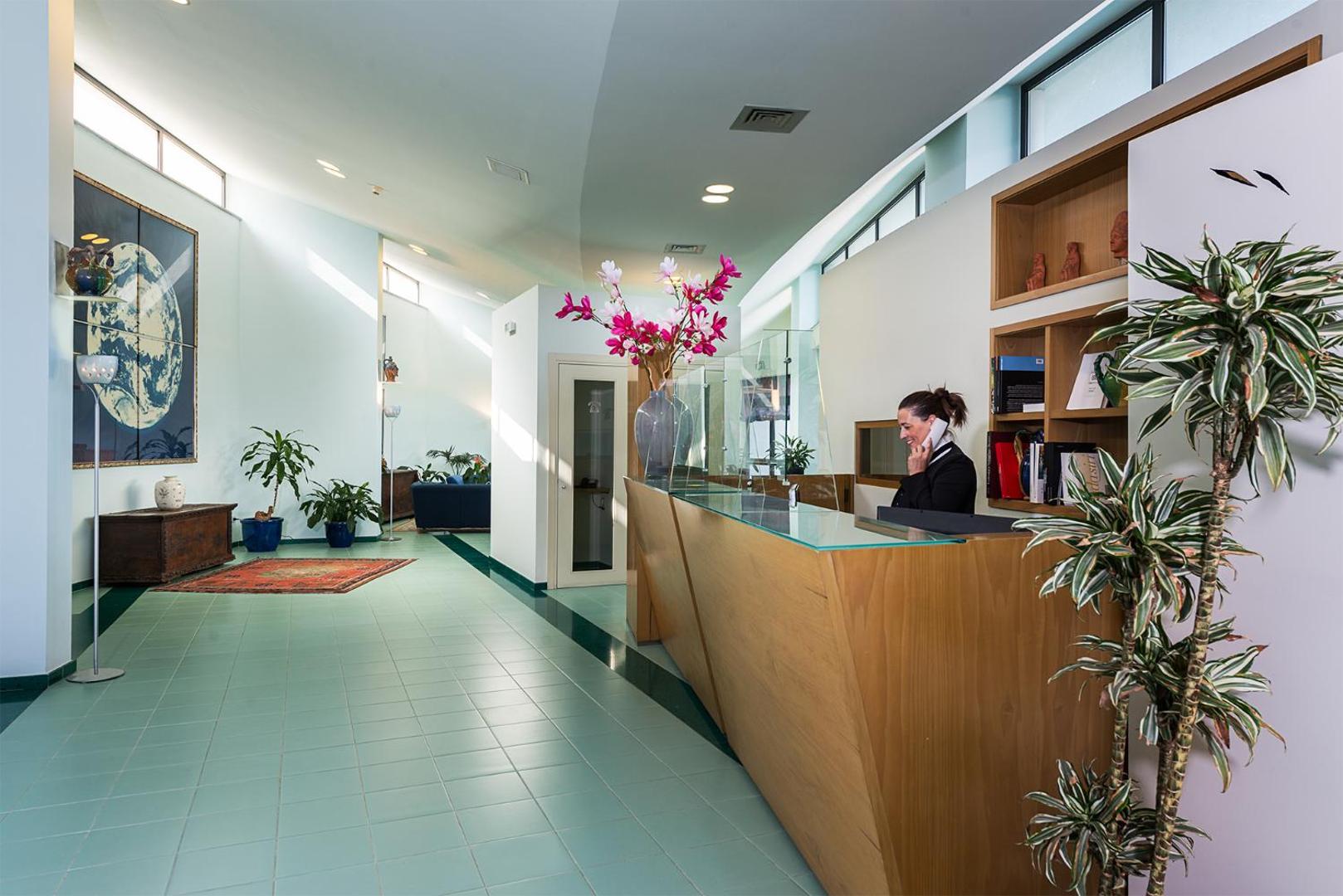 Rada Siri Hotel recepcijas zona ar koka leti, ziedu dekorācijām un gaišu interjeru Kalabrijas reģionā, Itālijā