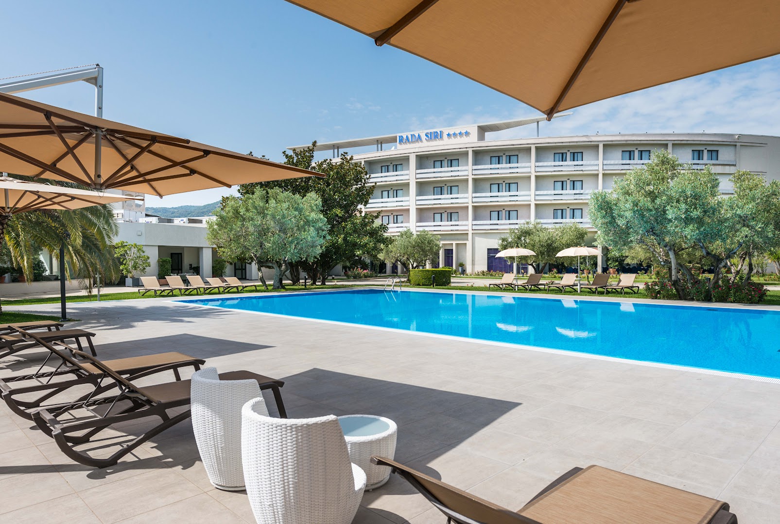 Viesnīcas Rada Siri Hotel baseina zona ar moderniem zviļņiem un saulessargiem pie galvenās ēkas Itālijā