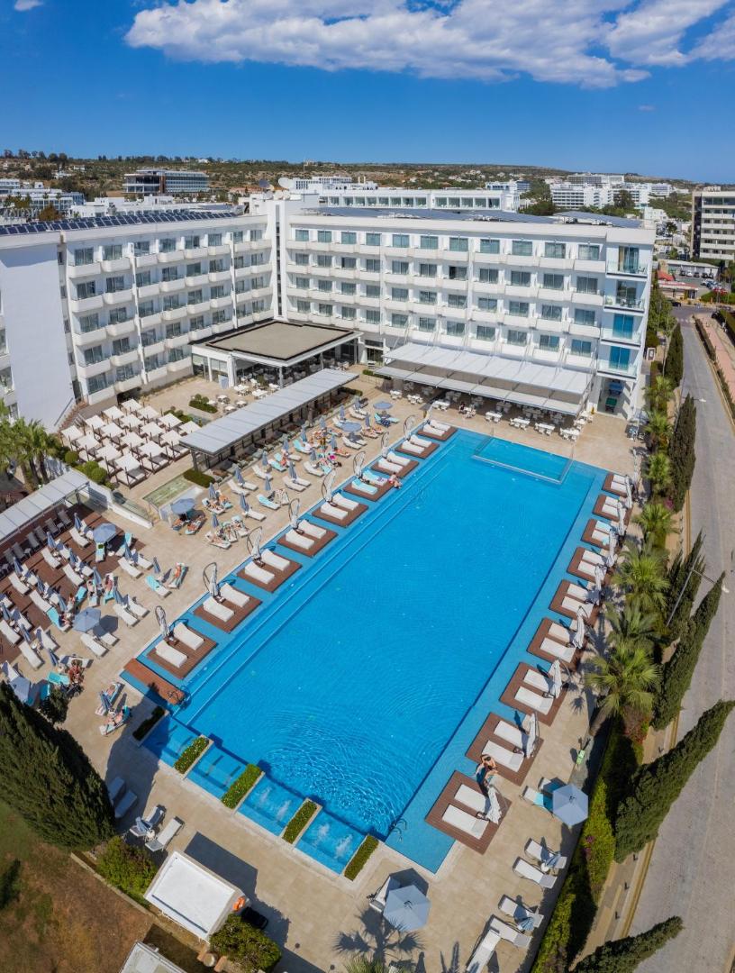 Nestor Hotel viesnīcas komplekss no augšas Aijanapā — liels peldbaseins, balta ēkas fasāde un sakopta apkārtne saulainā dienā