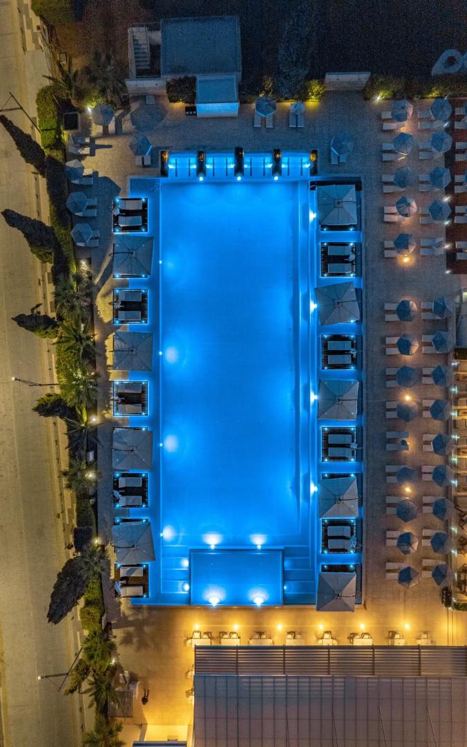 Nestor Hotel baseina skats no augšas naktī Aijanapā — simetrisks izkārtojums ar zilu apgaismojumu, saulessargiem un atpūtas zonām