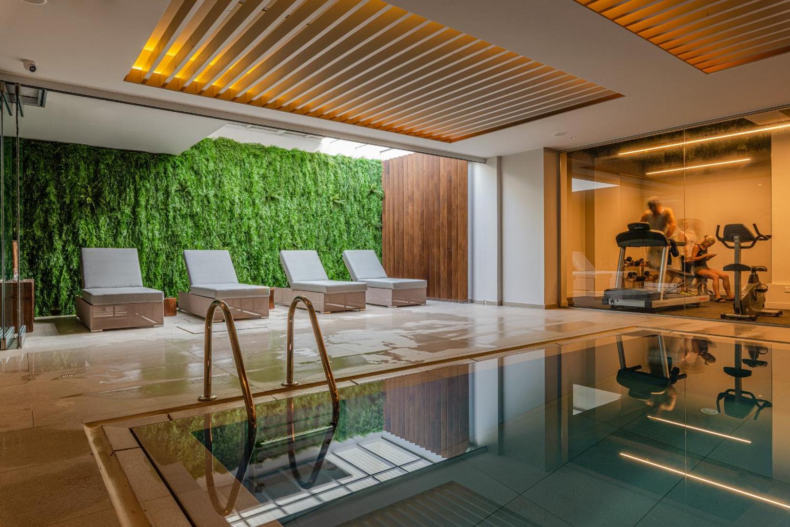 Nelia Beach spa zona ar iekštelpu baseinu, zviļņiem pie zaļās sienas un stiklotu fitness zāli fonā