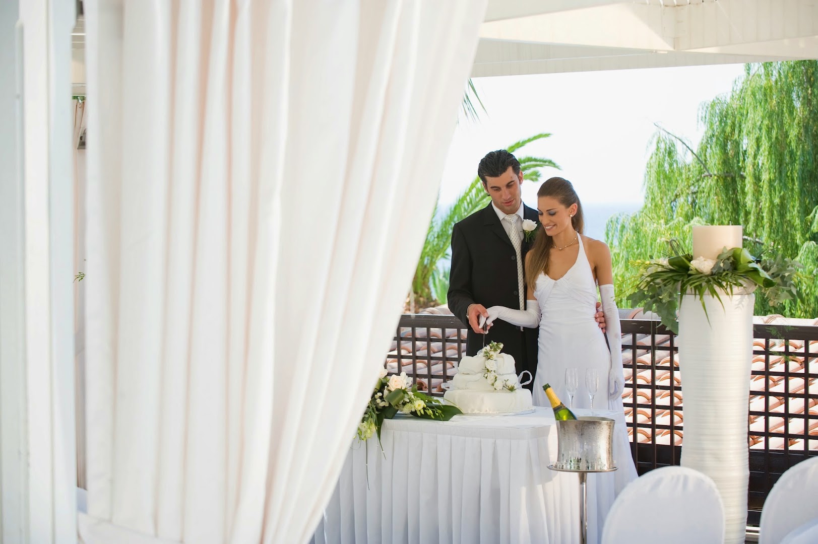 Kāzu ceremonija Mediterranean Beach Hotel terasē ar skatu uz jūru, jaunais pāris griež kūku pie svētku galda