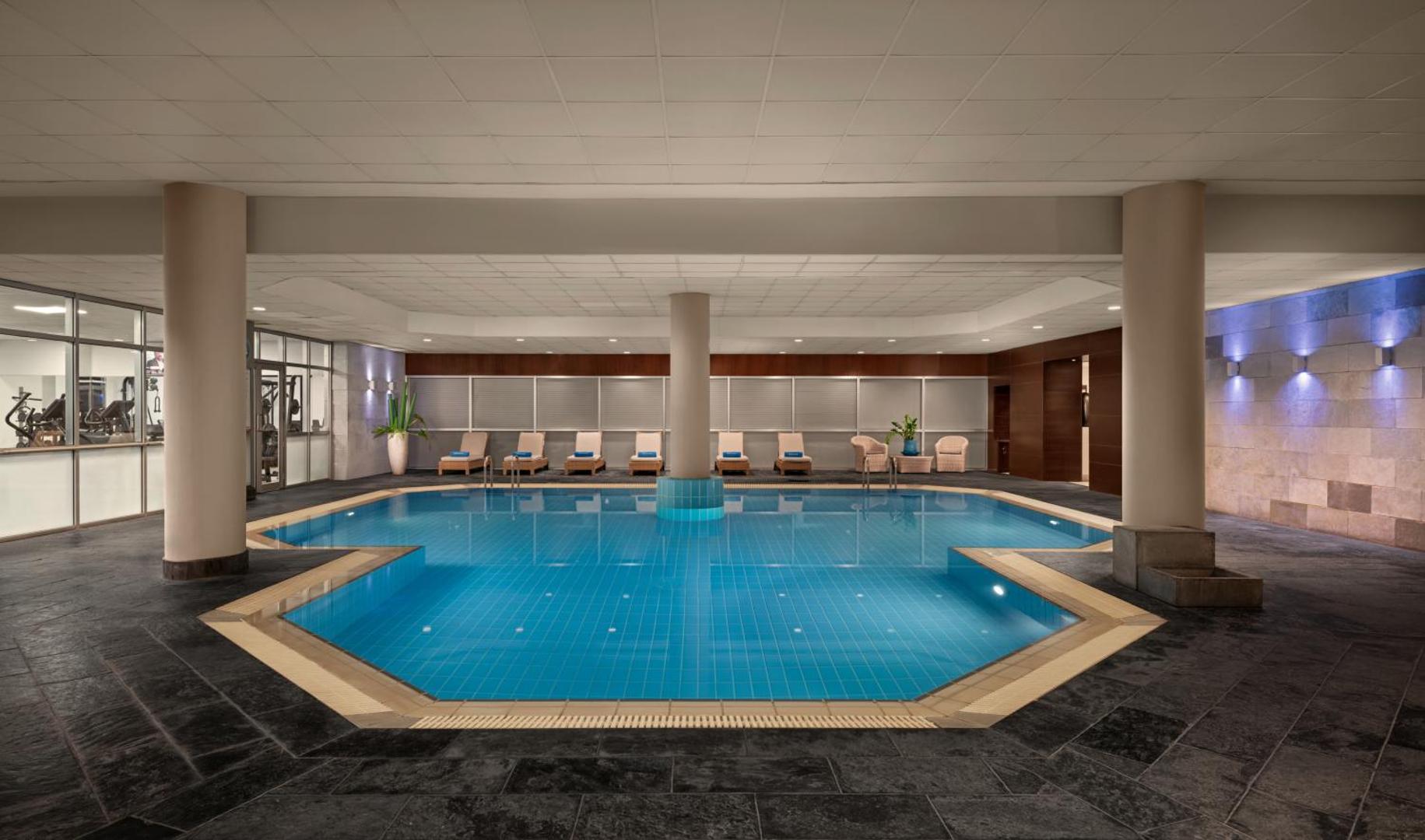Mediterranean Beach Hotel iekštelpu baseins ar apsildi un atpūtas krēsliem spa zonā, blakus redzama fitnesa zāle