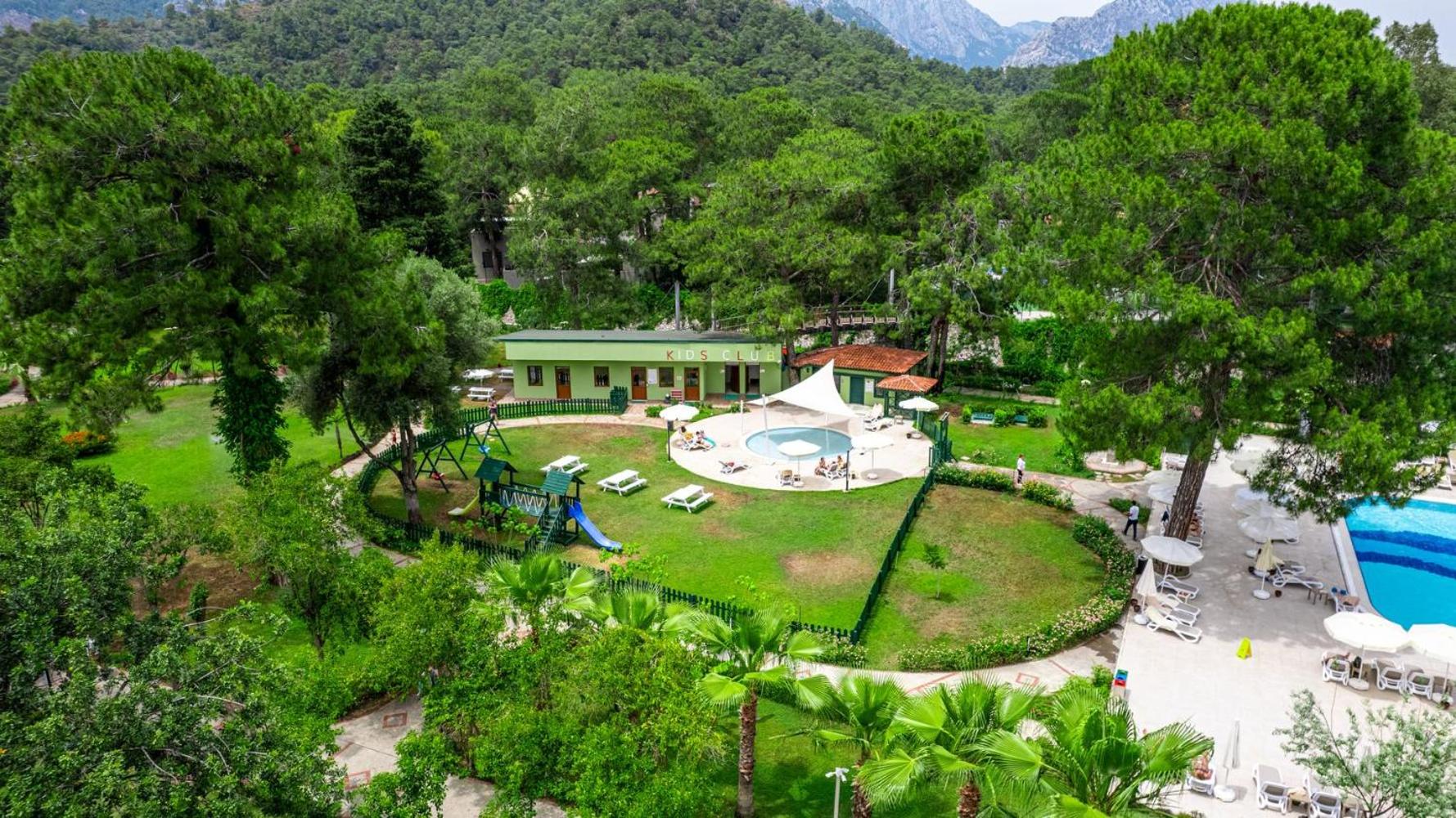 Aerofotoattēls ar viesnīcas bērnu klubu, rotaļu laukumu un baseinu zaļojošu priežu meža ieskāvumā.