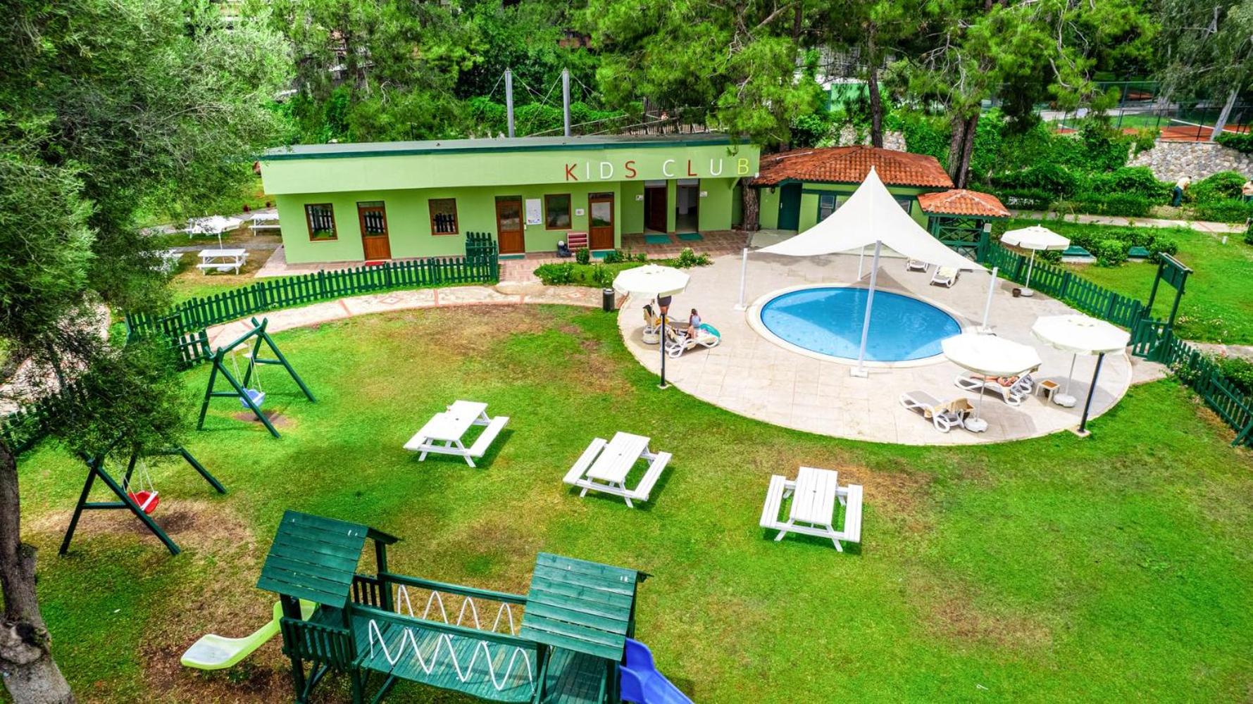 Bērnu kluba ēka ar nelielu baseinu, šūpolēm un sauļošanās krēsliem uz zālāja.