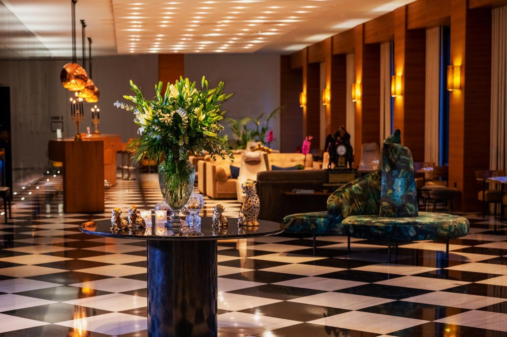 Viesnīcas vestibila interjers ar dizaina mēbelēm, ziediem un siltu apgaismojumu vakarā.