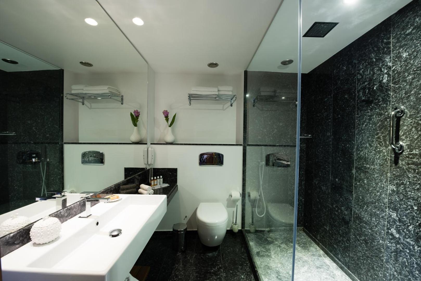 Gaiša vannas istaba ar plašu dušu, melna marmora apdari un lielu spoguli.