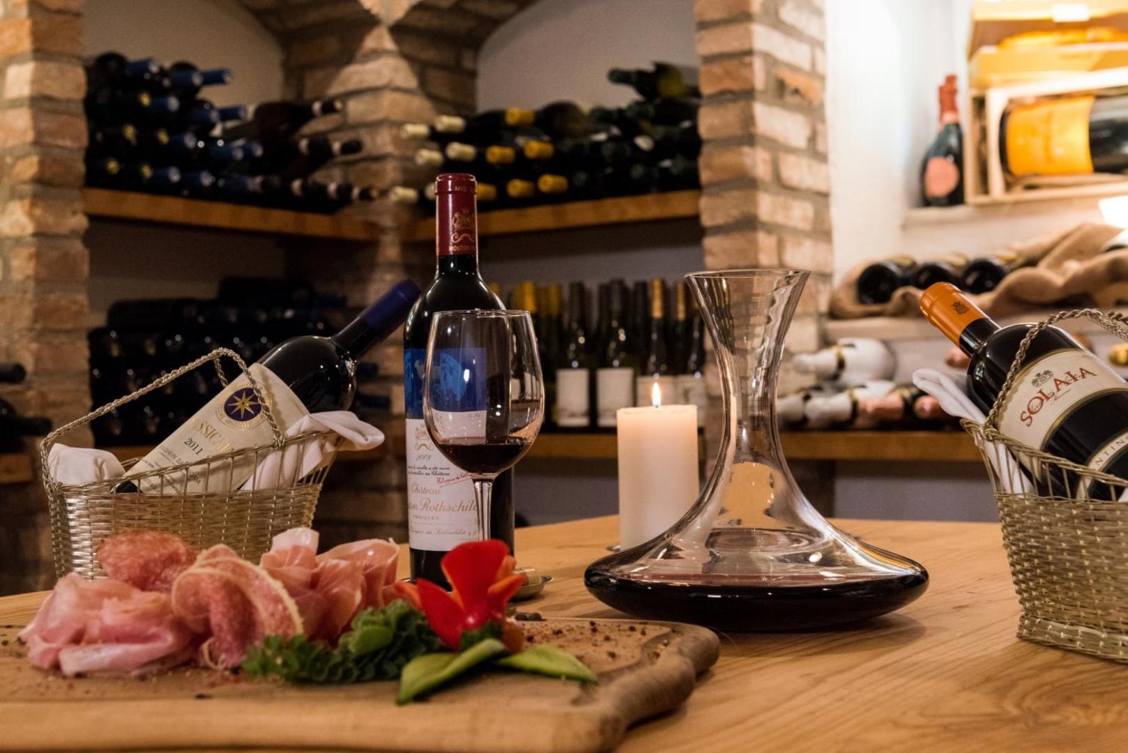 Vīna pagrabs ar izmeklētām vīna pudelēm, dekanteri un uzkodu plati.