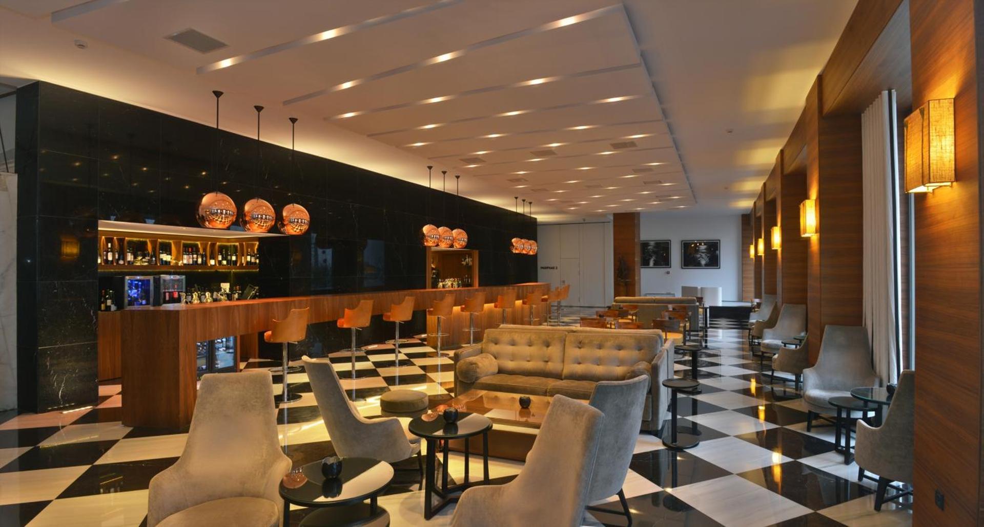 Plašs viesnīcas vestibila bārs ar modernām mēbelēm un melnbaltu rūtainu grīdu.