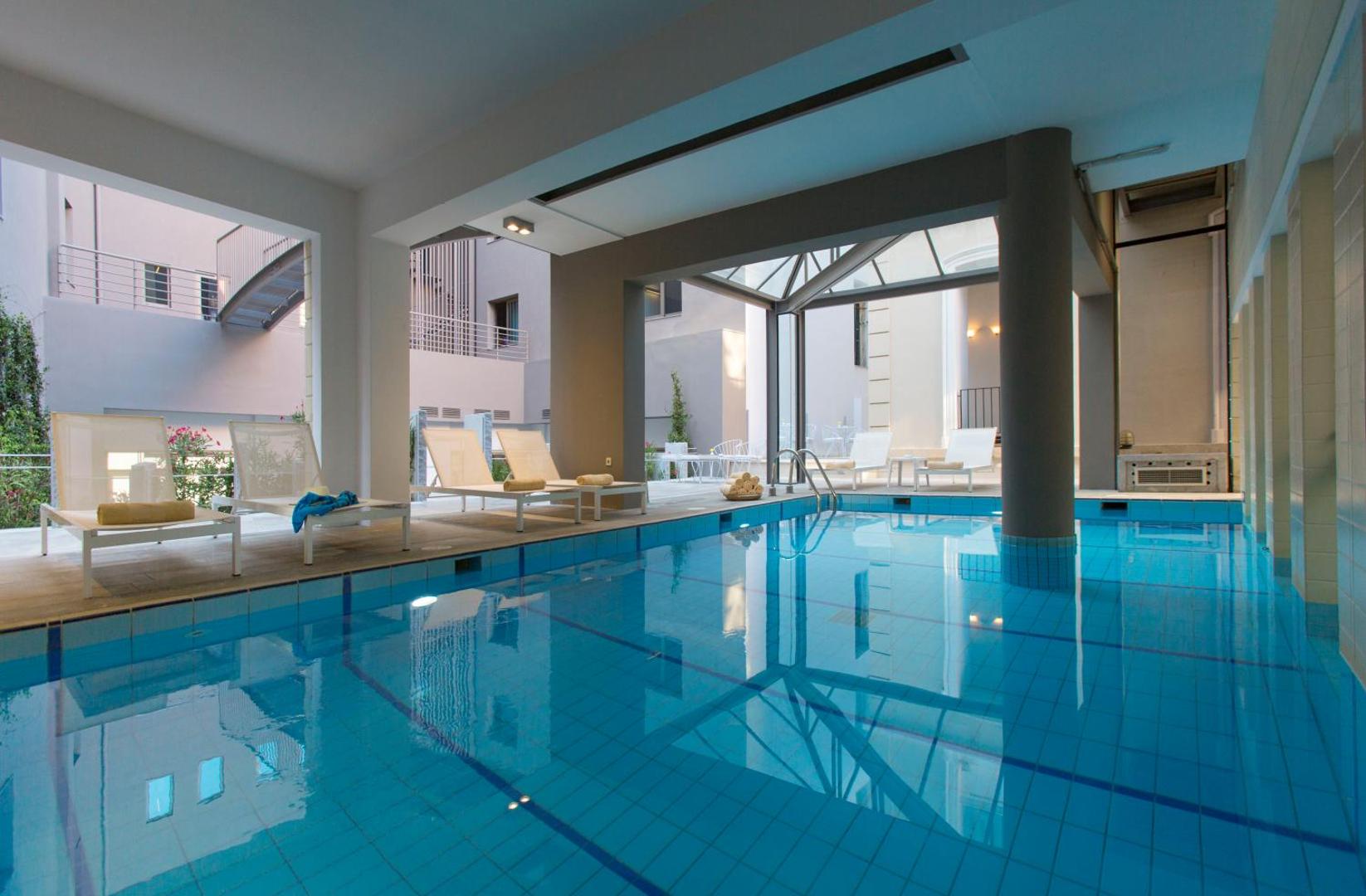 Iekštelpu baseins ar gaišiem sauļošanās krēsliem un modernu arhitektūru.