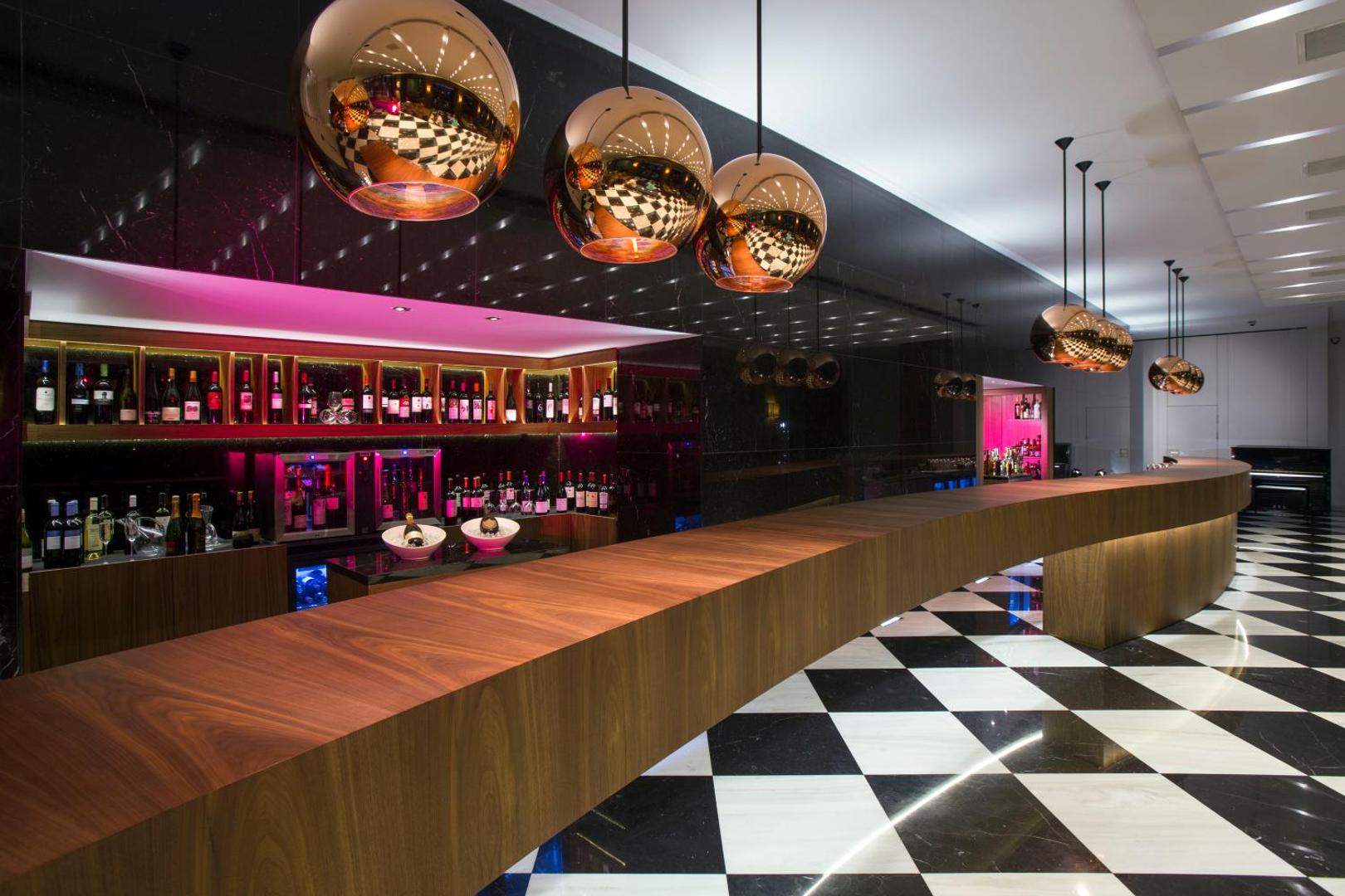 Moderns bārs ar garu koka leti, dizaina lampām un plašu vīnu izvēli.