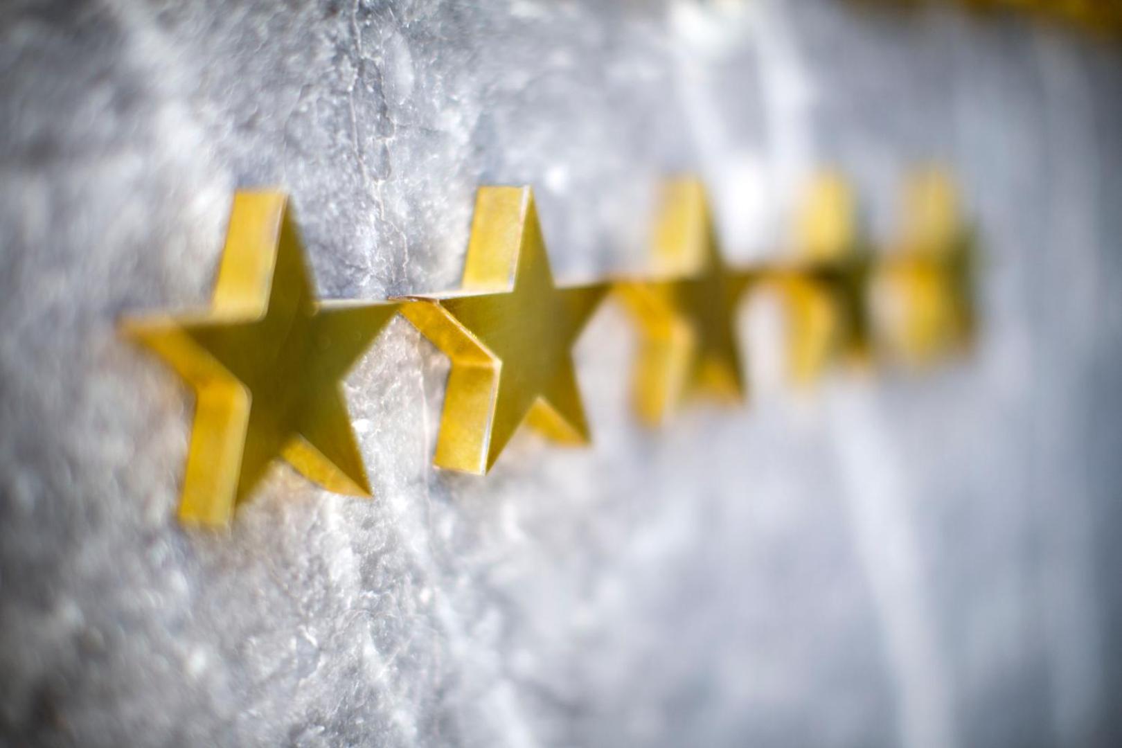 Piecas zelta krāsas zvaigznes uz pelēka akmens sienas fona tuvplānā.