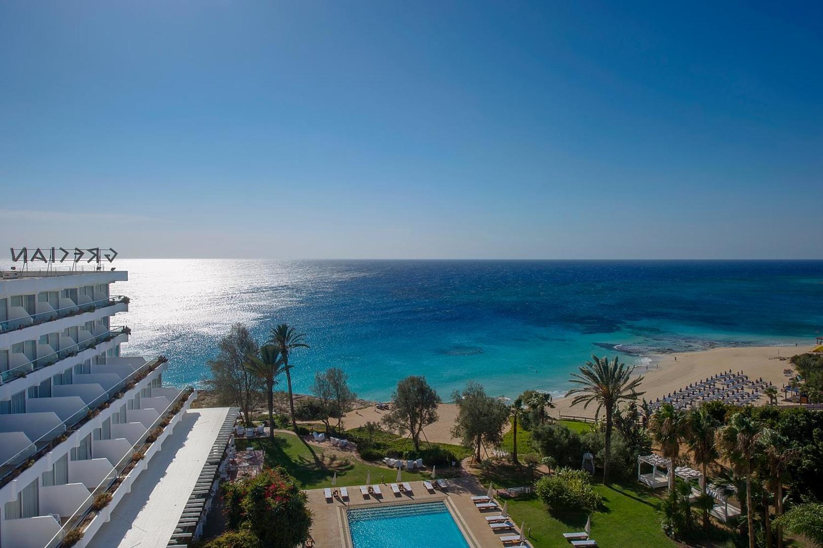 Grecian Sands viesnīcas ēka un baseins ar skatu uz smilšu pludmali un tirkīzzilo jūru Aijanapā, Kiprā