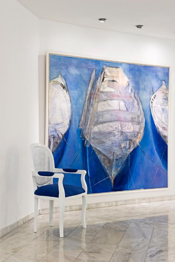 Interjera detaļa Grecian Sands viesnīcā ar zilu gleznu un stilīgu krēslu gaišā marmora hallē Ajanapā