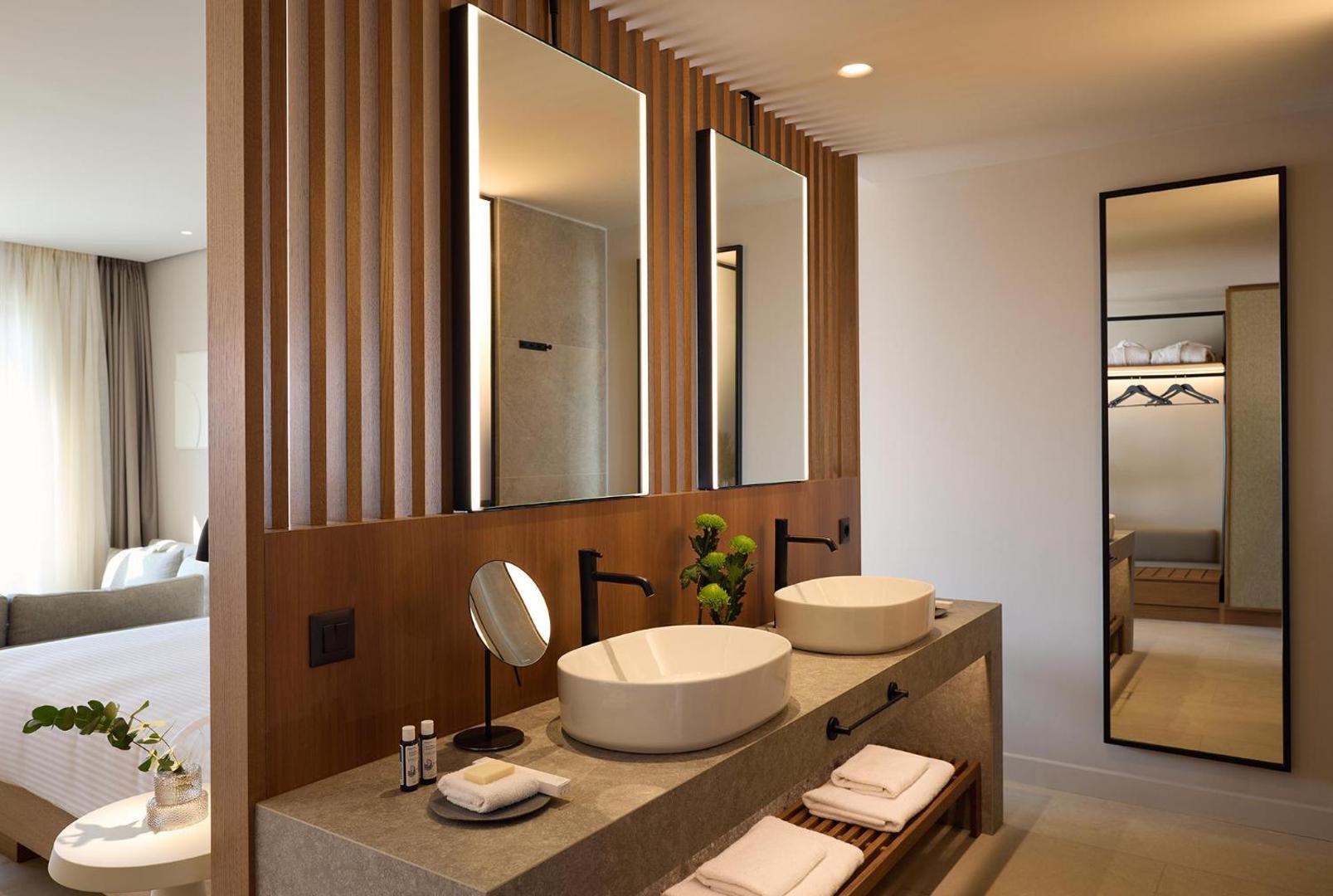 Moderna vannas istaba ar divām izlietnēm, koka apdari un lieliem, apgaismotiem spoguļiem.