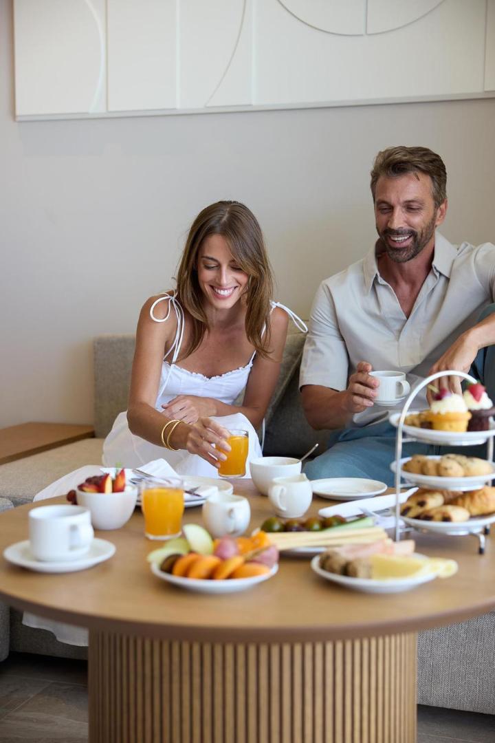 Smaidīgs pāris bauda brokastis un kafiju pie eleganti klāta galda viesnīcas numurā.