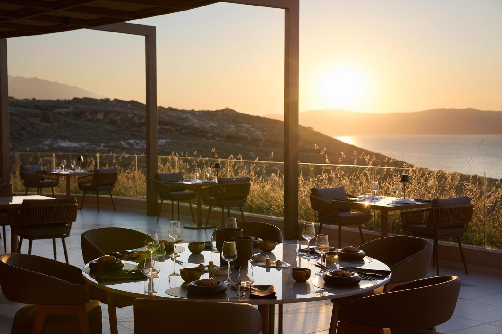 Viesnīcas restorāna terase ar klātiem galdiem saulrieta laikā ar skatu uz jūru.